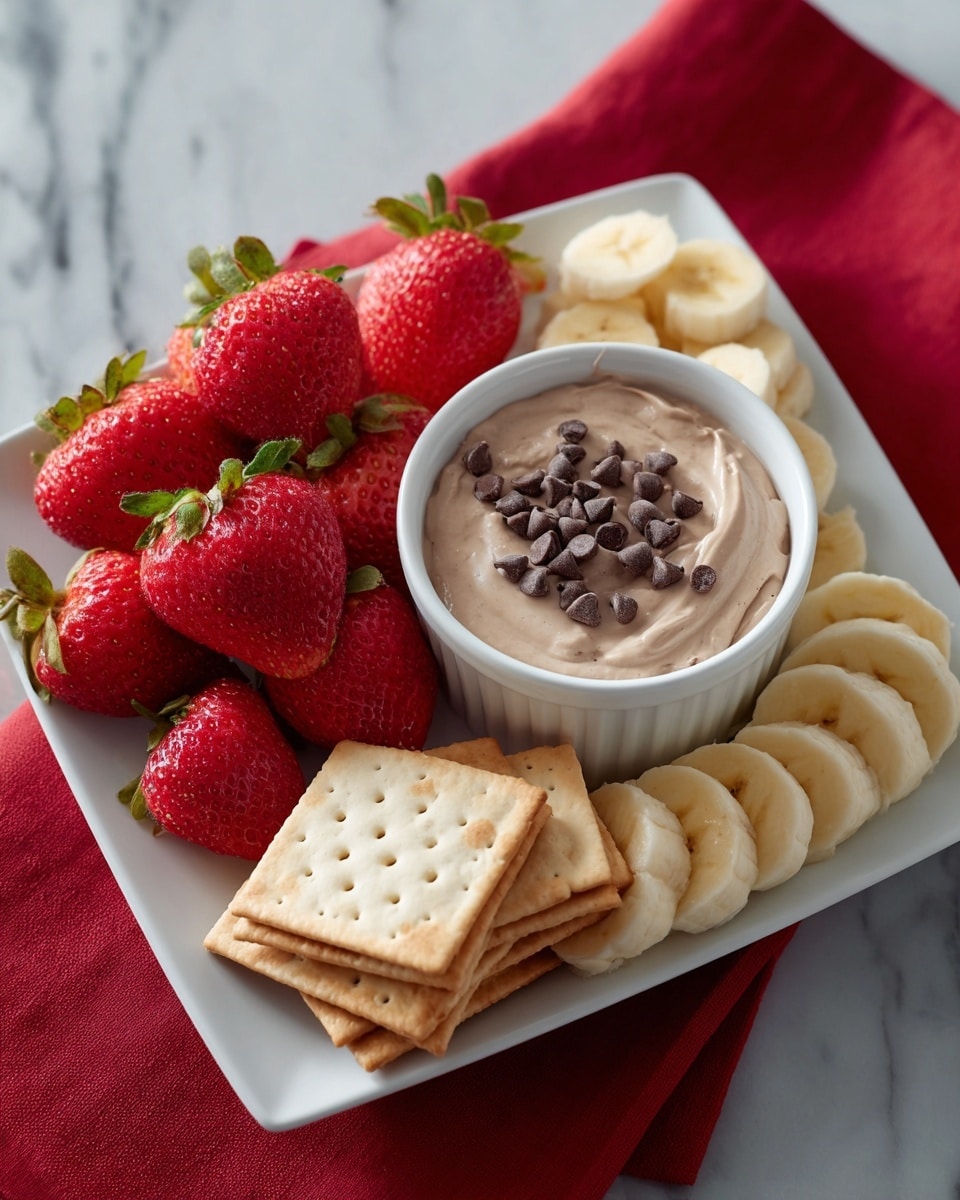 A white square plate is arranged with four groups of snacks: a cluster of bright red strawberries with green leaves, a row of banana slices showing light yellow color with soft texture, a neat stack of square light beige crackers with tiny holes, and a white round ramekin filled with a smooth light brown creamy dip topped with small dark brown chocolate chips. The plate is set on a red cloth on a white marbled surface. photo taken with an iphone --ar 4:5 --v 7