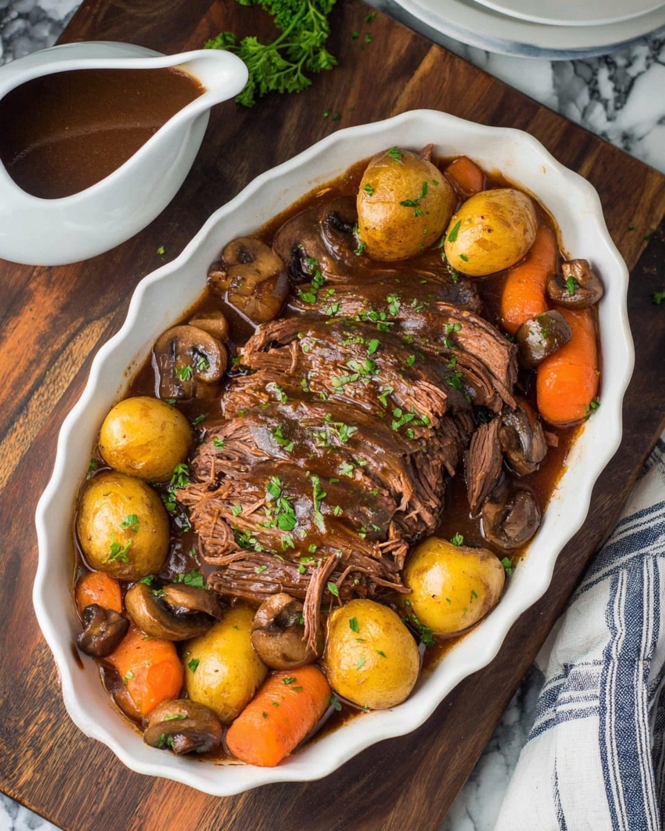 A white scalloped oval dish holds a hearty pot roast meal with three thick layers of shredded, brown cooked beef stacked in the center, topped with small bright green chopped herbs. Surrounding the beef are chunky golden baby potatoes, vibrant orange carrot slices, and whole brown mushrooms, all sitting in a dark brown rich gravy. To the left, a white gravy boat filled with more thick brown gravy is partially visible. The dish is placed on a dark wooden surface with a striped cloth peeking in from the right side, and the background shows a white marbled texture. Photo taken with an iphone --ar 4:5 --v 7