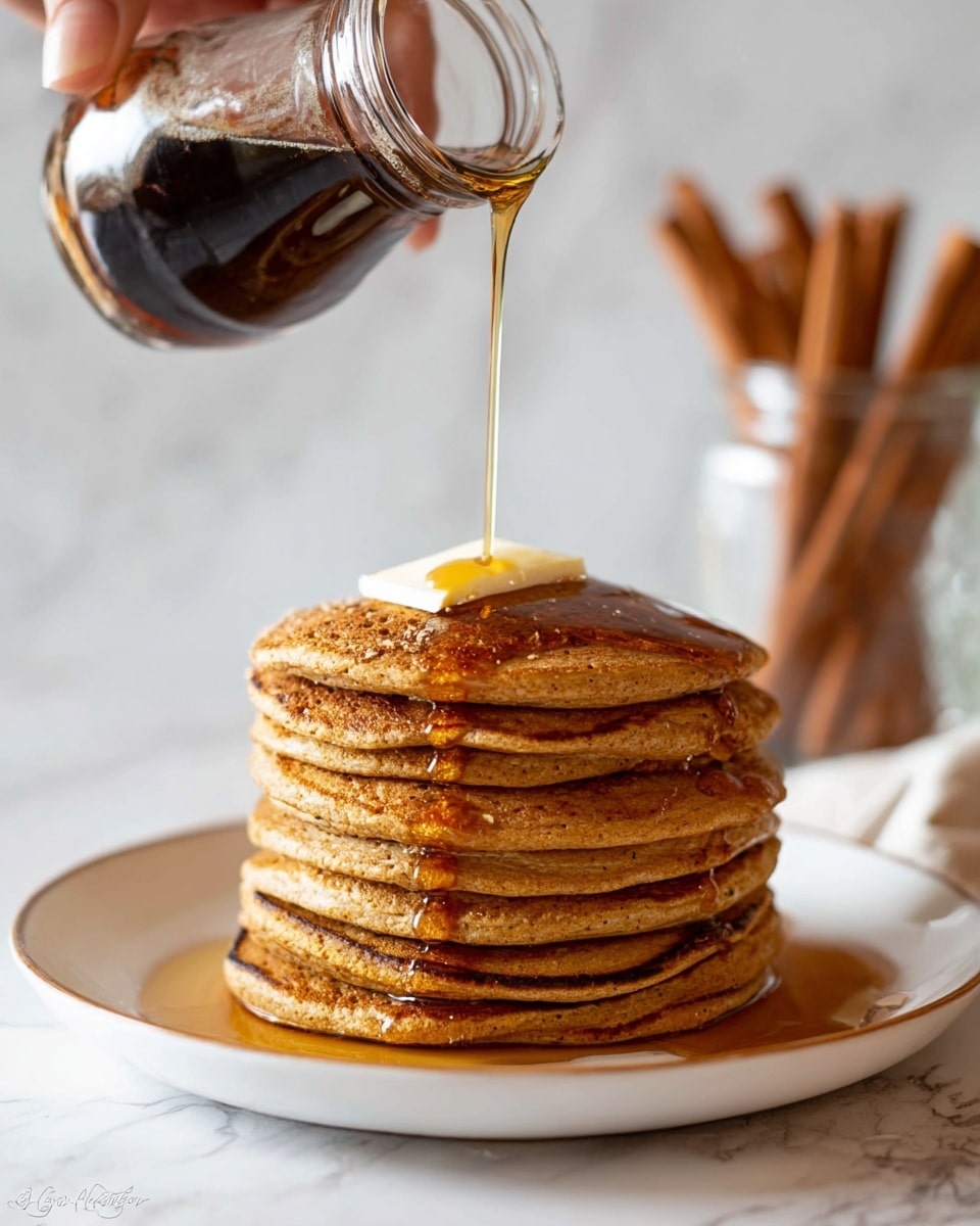 A tall stack of seven thick, golden-brown pancakes with a lightly textured surface sits at the center of a white plate. A small square of butter melts on the top pancake while a thin, dark amber syrup is poured from a clear glass jar held by a woman's hand, flowing down the sides of the stack and pooling slightly on the plate. The background shows blurred cinnamon sticks in a clear jar, all set on a surface with a white marbled texture. photo taken with an iphone --ar 4:5 --v 7