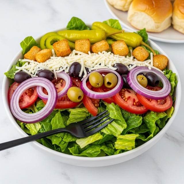 The image shows a fresh salad in a white bowl on a white marbled surface. The salad has several layers, starting with a base of green lettuce leaves that are crisp and leafy. On top, there are slices of red tomato and rings of purple onion placed evenly around the bowl. Scattered throughout are golden brown croutons with a crunchy texture. There are also slices of green jalapeño peppers adding a spicy touch, and the salad is sprinkled with shredded white cheese and black pepper for extra texture and seasoning. photo taken with an iphone --ar 4:5 --v 7