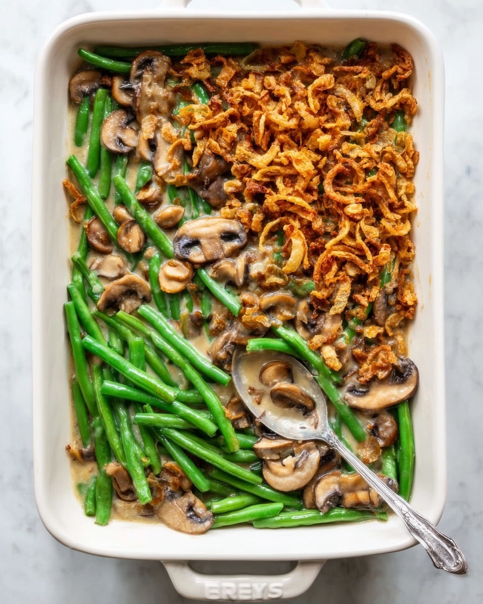 A white rectangular dish with three distinct layers of food neatly arranged inside; the top left section shows a layer of golden-brown crispy fried onions with small green bits scattered, the bottom right section contains steamed green beans mixed with sliced light brown mushrooms, and the top right section has a creamy white sauce with sliced mushrooms blending slightly with the green beans. A silver spoon rests on the right side of the dish. The background is a white marbled texture. Photo taken with an iphone --ar 4:5 --v 7