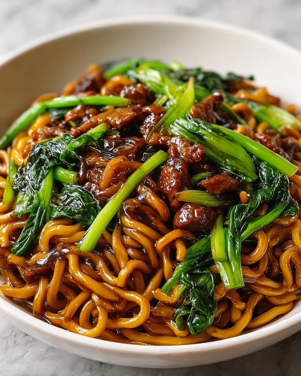 A round white bowl filled with three main layers: at the bottom, shiny, curly, thick yellow-orange noodles coated in sauce; on top of this, dark brown, glossy pieces of cooked meat scattered evenly; and mixed throughout and on the top, bright green leafy vegetables and light green stalks cut into short pieces, all sitting on a white marbled surface. photo taken with an iphone --ar 4:5 --v 7