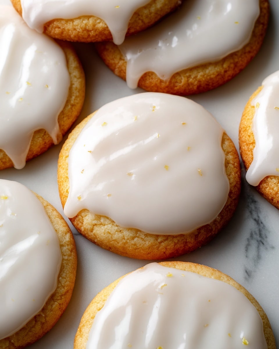 A close-up view of several soft, round cookies with a light golden base topped with a thick, smooth white glaze that evenly covers each cookie, slightly dripping down the sides. The cookies are placed close together on a white marbled surface, showing their fluffy and tender texture beneath the shiny glaze. photo taken with an iphone --ar 4:5 --v 7