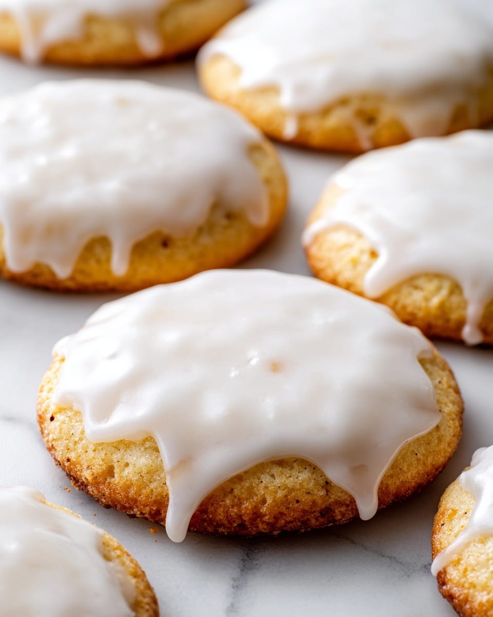 A close-up image showing a stack of soft, round cookies with a pale golden base and topped with thick, smooth white icing that slightly drips on the sides. The cookies have a slightly uneven shape and texture, highlighting their homemade look. They are laid out closely together on a white marbled surface. The icing covers the entire top of each cookie, creating a shiny and creamy layer that contrasts gently with the matte, soft-colored cookie base. Photo taken with an iphone --ar 4:5 --v 7