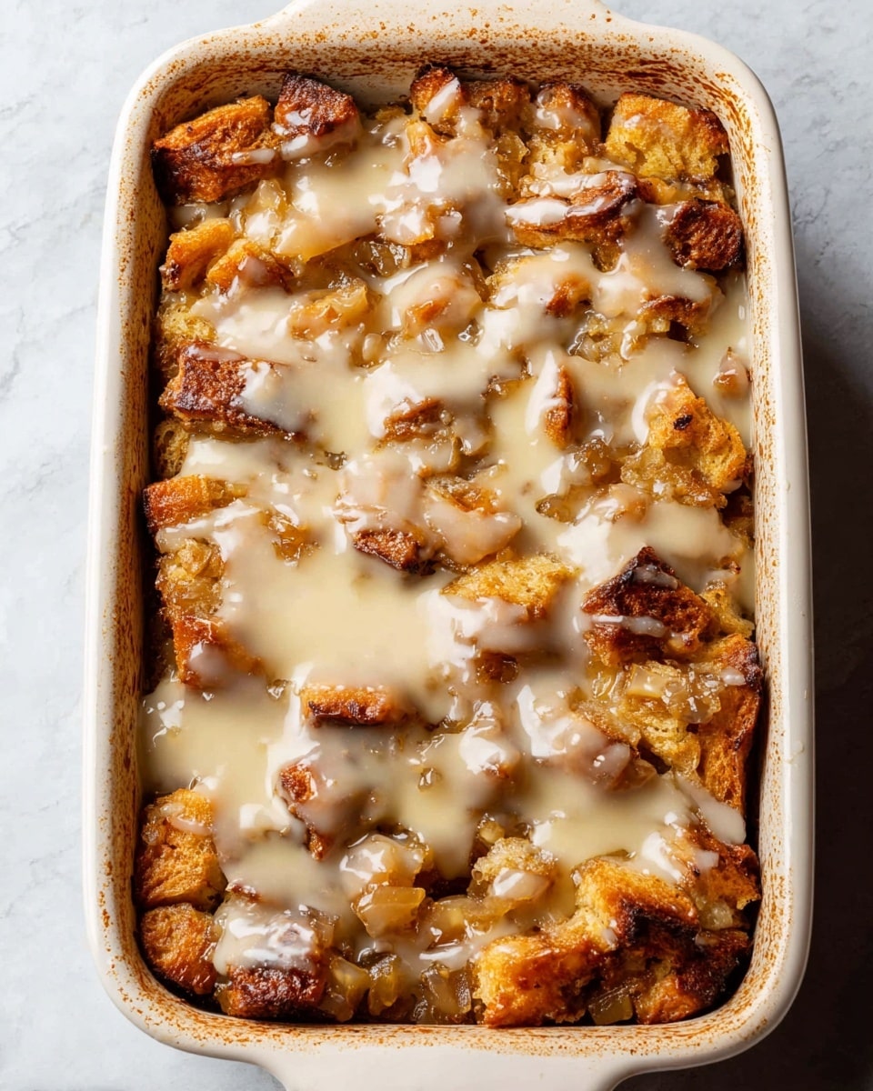 A baked dessert sits in a white rectangular baking dish with slightly browned edges. The dish is filled with a mix of soft, golden-brown bread pieces and caramelized chunks, topped with a smooth, creamy light beige glaze drizzled unevenly across the surface. The bread pieces have a textured, slightly rough look with some darker toasted spots, while the glaze adds a shiny, glossy finish. The background is a white marbled texture. photo taken with an iphone --ar 4:5 --v 7