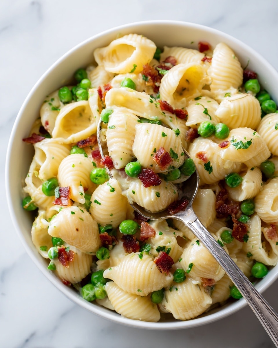 A close-up of a white bowl filled with pasta shells mixed with green peas and small pieces of crispy bacon. The pasta shells are creamy and light yellow, coated in a smooth sauce. Bright green peas are scattered throughout, adding a fresh contrast, while bits of browned bacon add texture and color. A silver spoon lifts a portion of the pasta, showing the mix of all ingredients clearly on the spoon, against a white marbled background. Photo taken with an iphone --ar 4:5 --v 7