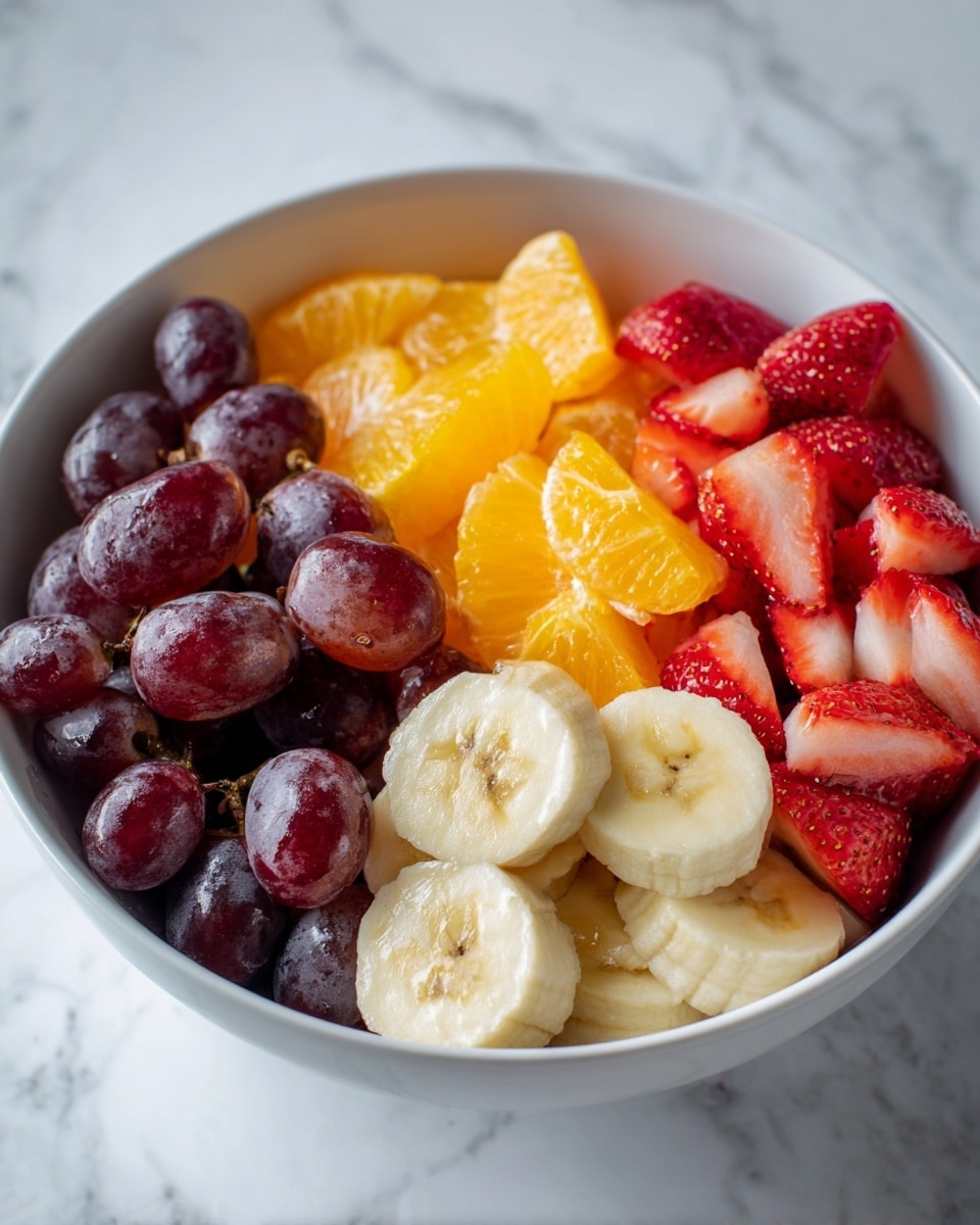 A white bowl filled with a colorful fruit salad showing distinct layers: at the base, thick slices of yellow banana with soft texture and visible seeds, sitting close to large, bright orange chunks of juicy pineapple in the middle, topped with red strawberry pieces that have a seed-studded smooth surface, and clustered on one side are dark purple, shiny grapes creating a contrast in color and texture. The bowl is placed on a white marbled texture surface. photo taken with an iphone --ar 4:5 --v 7