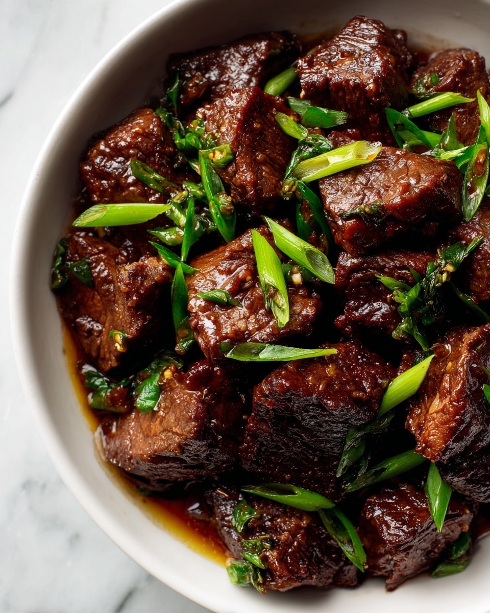 A close-up of a white bowl filled with glossy dark brown beef chunks cooked in a rich sauce, showing visible texture and slight marbling on the beef pieces. Bright green chopped scallions are scattered evenly on top, adding a fresh color contrast. The beef pieces are thick and juicy, sitting in a shiny, thick sauce that pools slightly at the bottom of the bowl. The white bowl is set on a white marbled textured surface. photo taken with an iphone --ar 4:5 --v 7