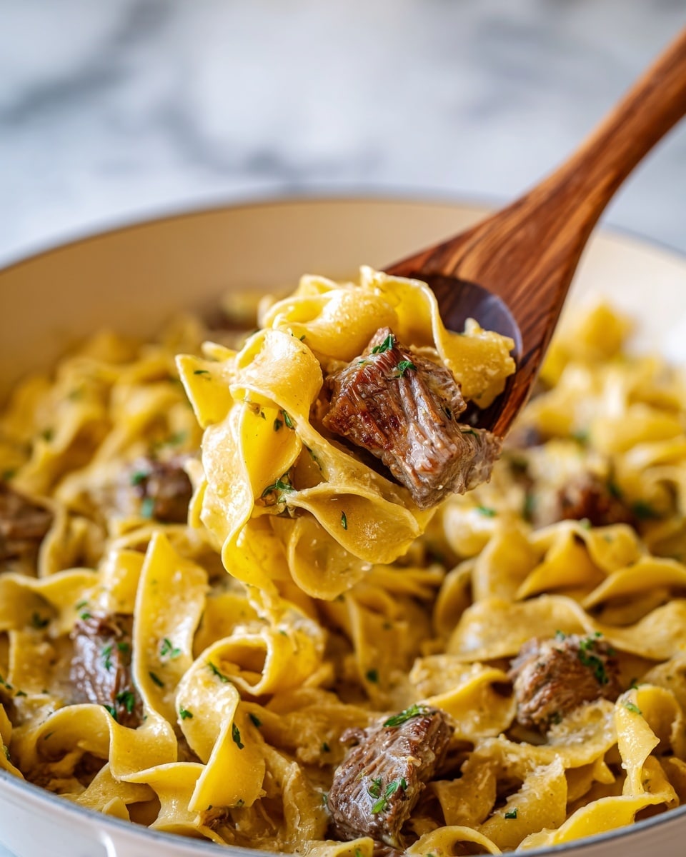 A close-up image of a wooden spoon lifting a portion of wide, flat pasta noodles mixed with small chunks of browned meat, coated in a creamy sauce with green herb bits sprinkled evenly on top. The pasta is pale yellow with a smooth texture, while the meat pieces are brown with a slightly crispy look. The background shows more of the same pasta and meat in a white bowl with a creamy sauce, all placed on a white marbled surface. photo taken with an iphone --ar 4:5 --v 7