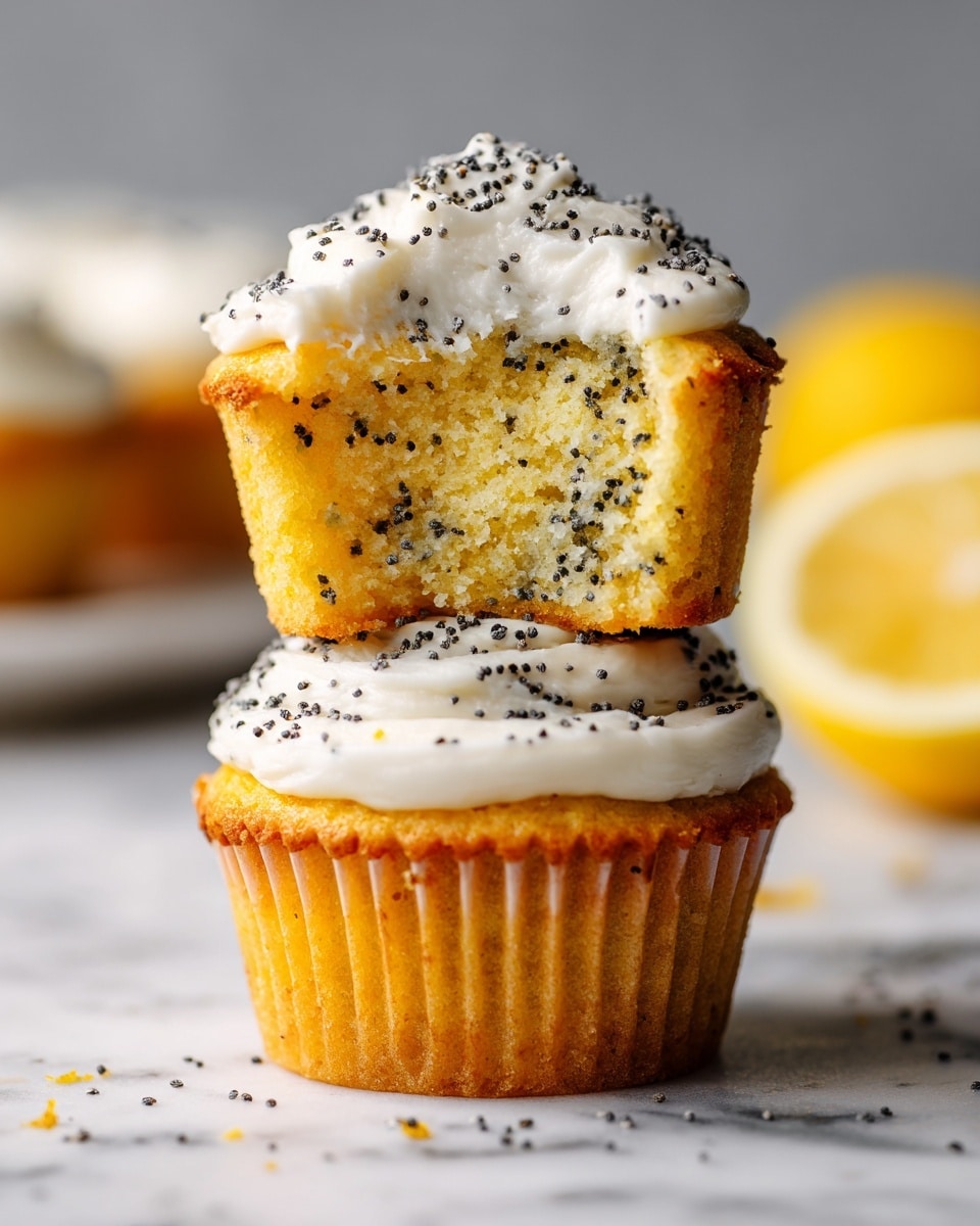 The image shows two lemon poppy seed cupcakes stacked on a white marbled surface. The bottom cupcake has a light golden-brown base with a white creamy frosting layer on top, sprinkled with tiny black poppy seeds. The cupcake above it has a bite taken out, revealing a soft yellow crumb with black poppy seeds mixed inside. This top cupcake is also covered with the same white frosting and poppy seed topping. In the background, a blurred half lemon adds a bright yellow accent. Photo taken with an iphone --ar 4:5 --v 7