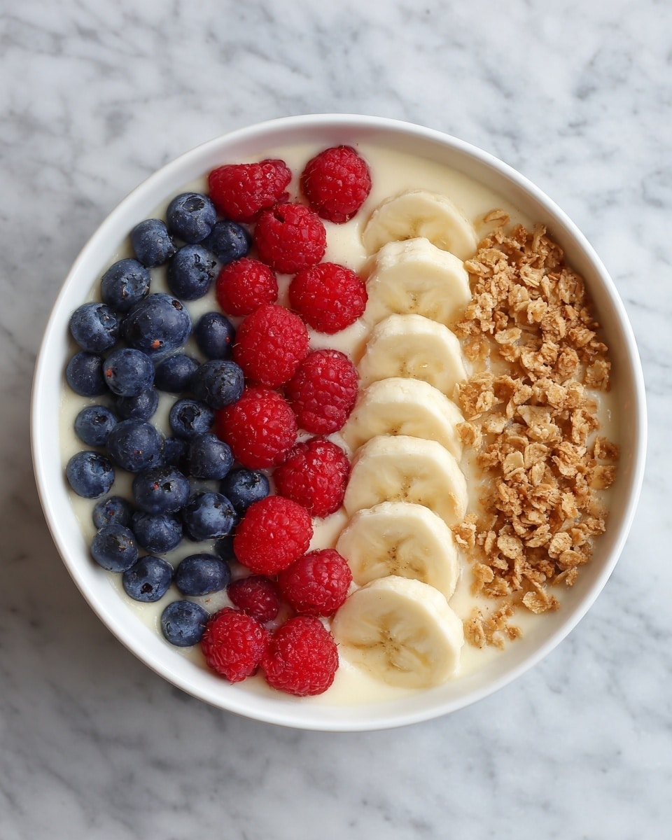 A white bowl filled with a smooth, creamy base topped with three neat rows of fresh fruits and toppings: bright red raspberries on one side, deep blue blueberries next to them, and thinly sliced banana pieces arranged in a curved line. In the middle row, there is a layer of crunchy granola with a light brown color creating a textured look. The bowl is placed on a white marbled surface. photo taken with an iphone --ar 4:5 --v 7