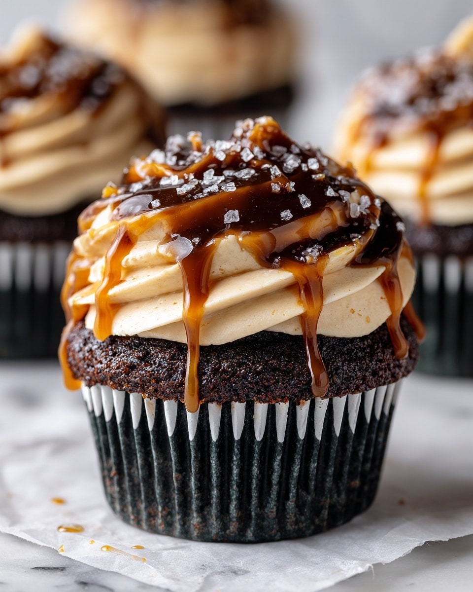 A close-up view of a rich dark chocolate cupcake with three distinct layers: the bottom layer is a dark, moist chocolate cake in a white cupcake liner; above it is a thick swirl of smooth, creamy light beige frosting; the top layer features glossy dark chocolate and golden caramel sauces drizzled generously, with small flakes of sea salt sprinkled on the frosting and sauces. The cupcake sits on a piece of white parchment paper, with a white marbled surface beneath. Photo taken with an iphone --ar 4:5 --v 7