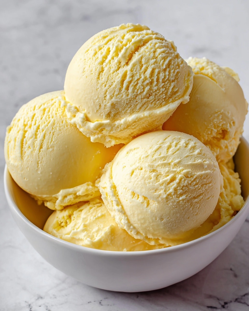 A close-up image showing multiple scoops of pale yellow ice cream stacked in a white bowl, each scoop smooth with slight creamy folds and small ridges. The texture looks soft and creamy, with subtle shadows giving depth to the rounded shapes. The background is a white marbled surface that softly contrasts with the ice cream's light color. photo taken with an iphone --ar 4:5 --v 7