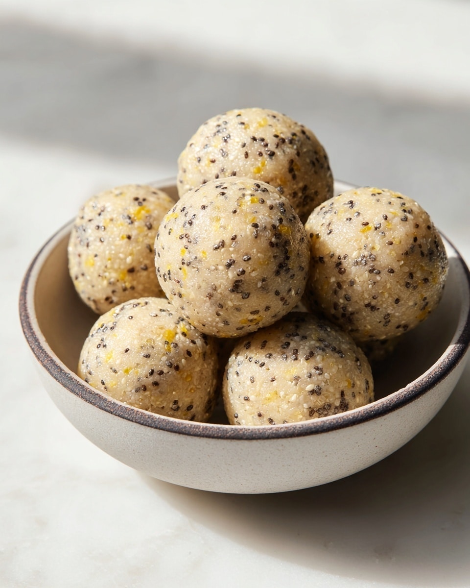 A close-up image of seven round energy balls in a simple white bowl with a slightly rough dark rim; each ball is pale cream in color with visible black chia seeds and small yellow bits mixed throughout, giving a speckled texture. The balls look dense and moist with a finely grained surface, piled so that three balls are clearly visible on top and the rest fill the bowl beneath. The bowl sits on a white marbled surface with soft light illuminating the scene from the side, highlighting the texture on the balls and the subtle speckles on the bowl. photo taken with an iphone --ar 4:5 --v 7