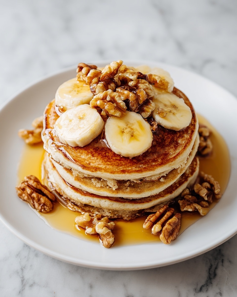 A stack of four thick, fluffy pancakes with a golden-brown color sits on a white plate, placed on a white marbled surface. The pancakes have a soft but slightly textured look, showing spots of cinnamon or nut filling inside the layers. The top pancake is covered with several walnut halves and banana slices, while whole walnuts are scattered around the base of the stack. A golden syrup glistens on and around the pancakes, pooling slightly on the white plate. photo taken with an iphone --ar 4:5 --v 7