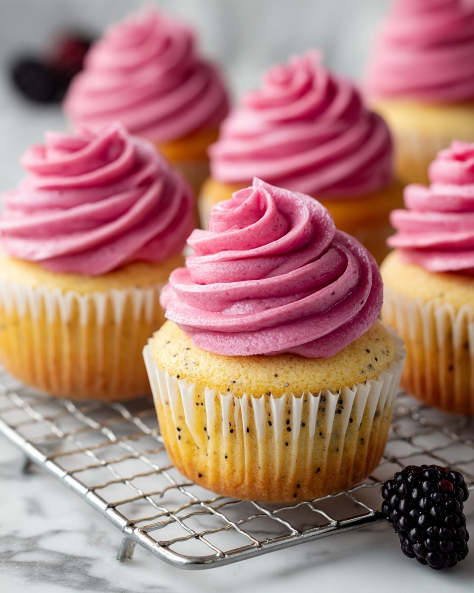 The image shows five cupcakes with two clear layers: the bottom cake layer is light yellow with tiny black seeds scattered throughout, sitting in ridged white paper liners, and the top layer is a thick swirl of smooth, bright pink frosting that looks creamy and slightly shiny, piped high in a spiral pattern. The cupcakes are placed on a silver cooling rack with a white marbled background visible beneath and behind them. A fresh, dark purple blackberry sits beside the rack in the lower right corner, adding a fresh contrast to the scene. Photo taken with an iphone --ar 4:5 --v 7